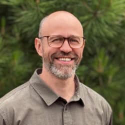 Ben Dixon, Principal Acoustics Consultant at Create Consulting Engineers, smiling outdoors against a green foliage background.