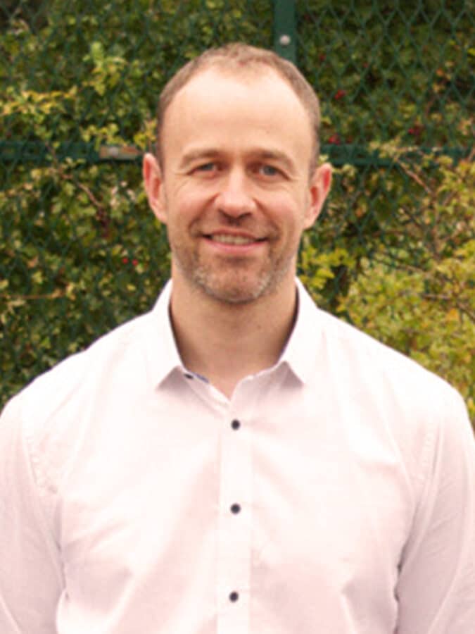 Ben Dixon, consulting engineer at Create Consulting Engineers, wearing a white shirt against a green foliage background.