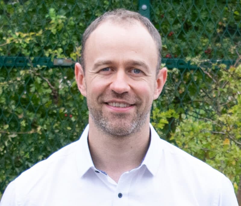 Ben Dixon, consultant at Create Consulting Engineers, wearing white shirt against green foliage background