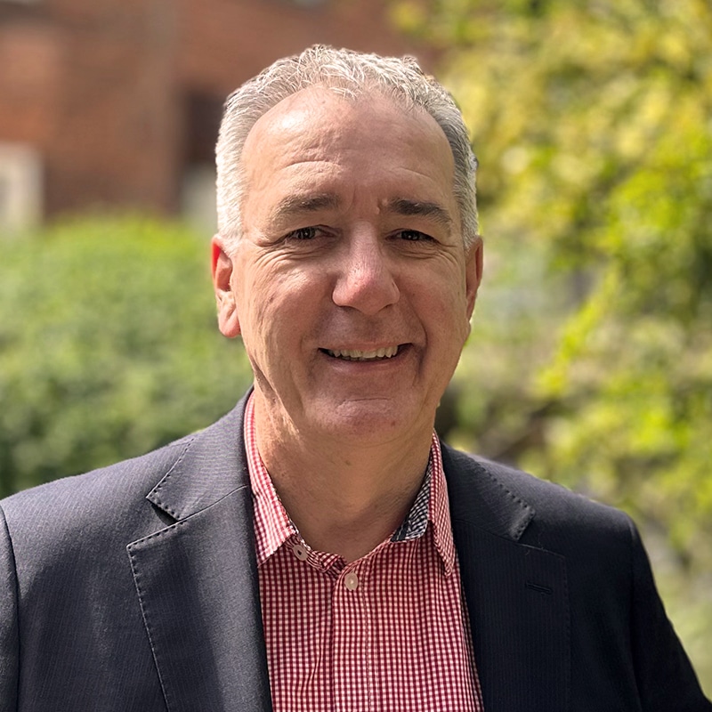Jonathan Cage, consultant at Create Consulting Engineers, smiling outdoors in professional attire with brick building and greenery background.