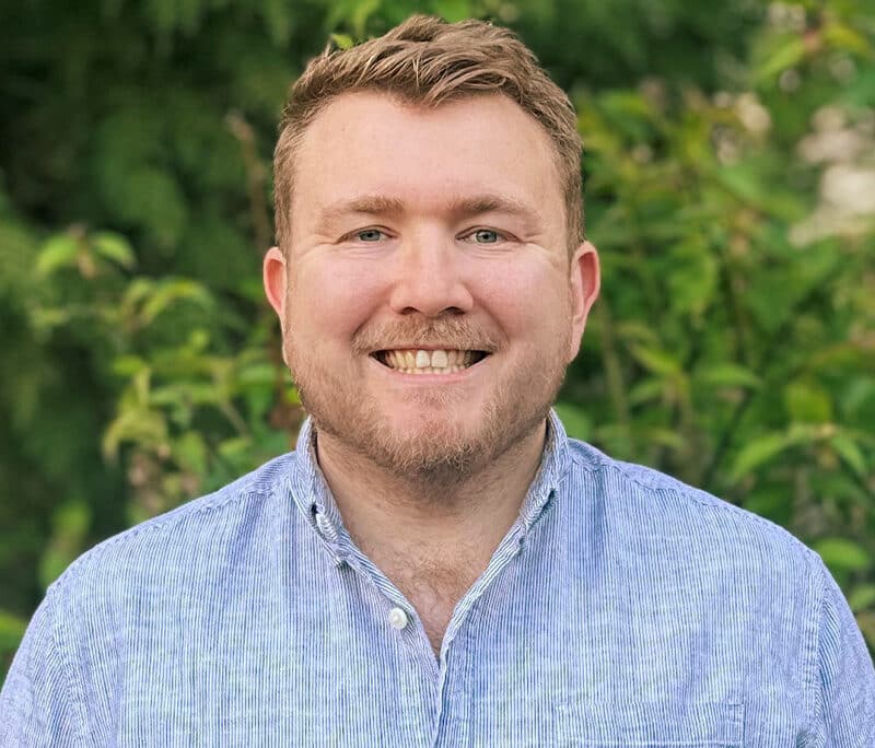 Jonathan Cage, engineering consultant at Create Consulting Engineers, smiling outdoors against green foliage background.