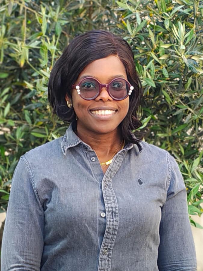 Bomi Ogunade, Create Consulting Engineers consultant, smiling outdoors wearing denim shirt and purple-tinted glasses.