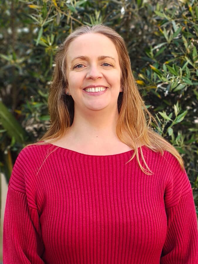 Claire Seymour, Practice Manager at Create Consulting Engineers, pictured in professional headshot wearing red ribbed jumper against foliage background.
