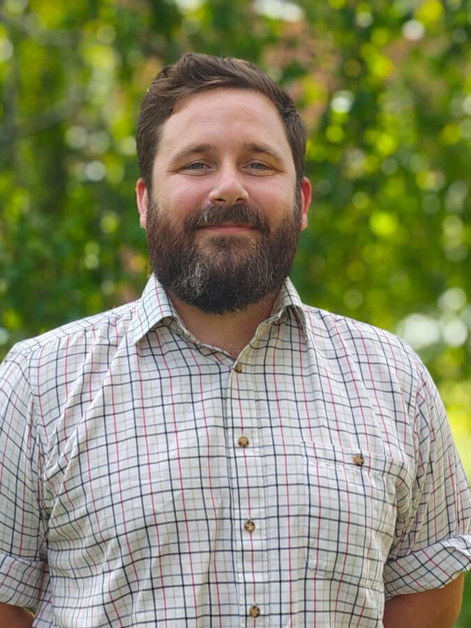 Bomi Ogunade, consulting engineer at Create Consulting Engineers, wearing checkered shirt against green foliage background.