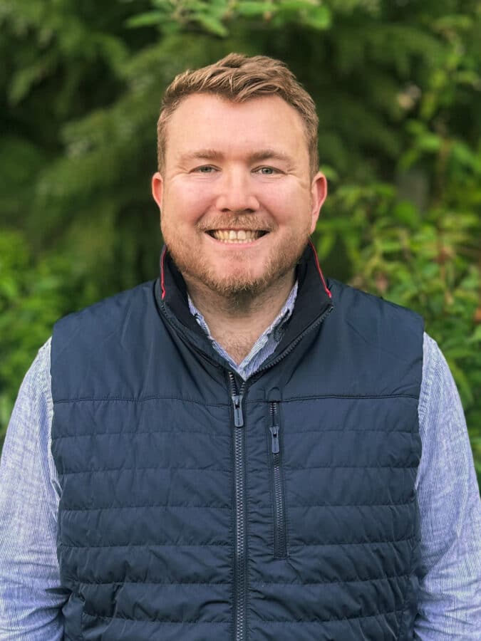 Matthew Wellington, Brand, Marketing and Proposals Manager at Create Consulting Engineers, smiling outdoors wearing navy gilet and light blue shirt.