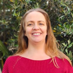 Professional headshot of a team member at Create Consulting Engineers, smiling at camera against green foliage background, wearing pink ribbed top.