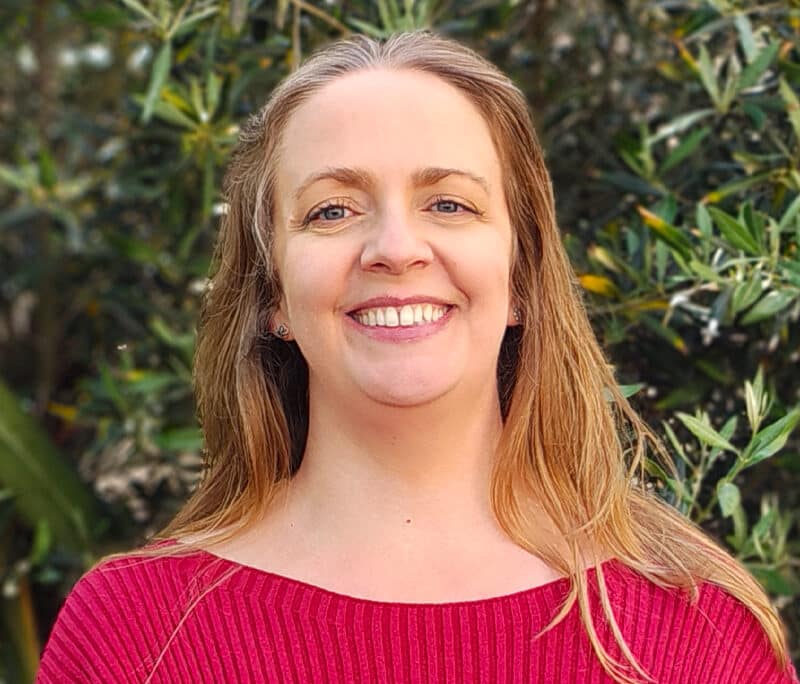 Professional headshot of a team member at Create Consulting Engineers, smiling at camera against green foliage background, wearing pink ribbed top.