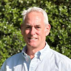Professional headshot of Simon Louis, engineering consultant at Create Consulting Engineers, outdoors with green foliage background.