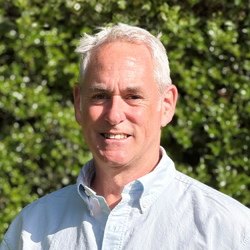 Professional headshot of Simon Louis, engineering consultant at Create Consulting Engineers, outdoors with green foliage background.