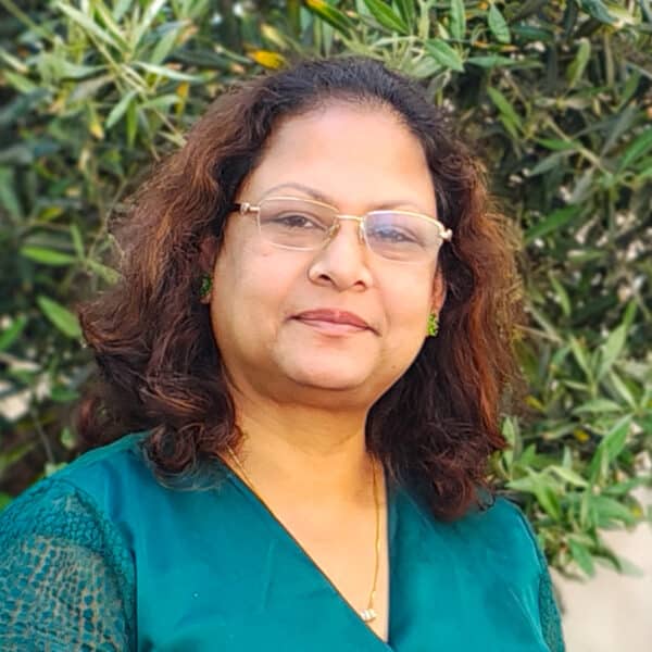 Professional portrait of a woman wearing glasses and teal top against green foliage background