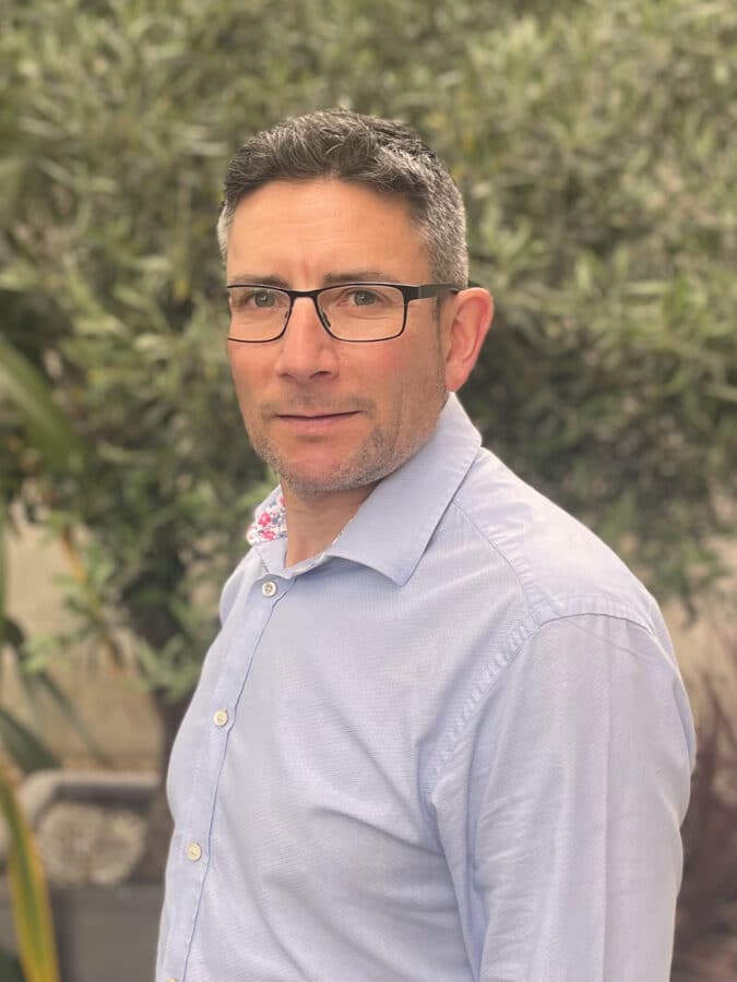 Andrew Warren, consulting engineer at Create Consulting Engineers, wearing light blue shirt and glasses against foliage background.