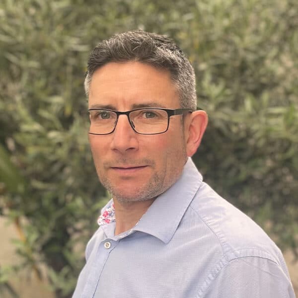 Andrew Warren, consultant at Create Consulting Engineers, wearing glasses and light blue shirt against foliage background.