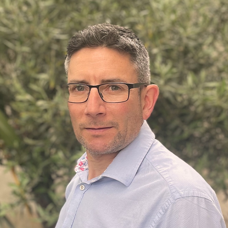 Andrew Warren, consultant at Create Consulting Engineers, wearing glasses and light blue shirt against foliage background.