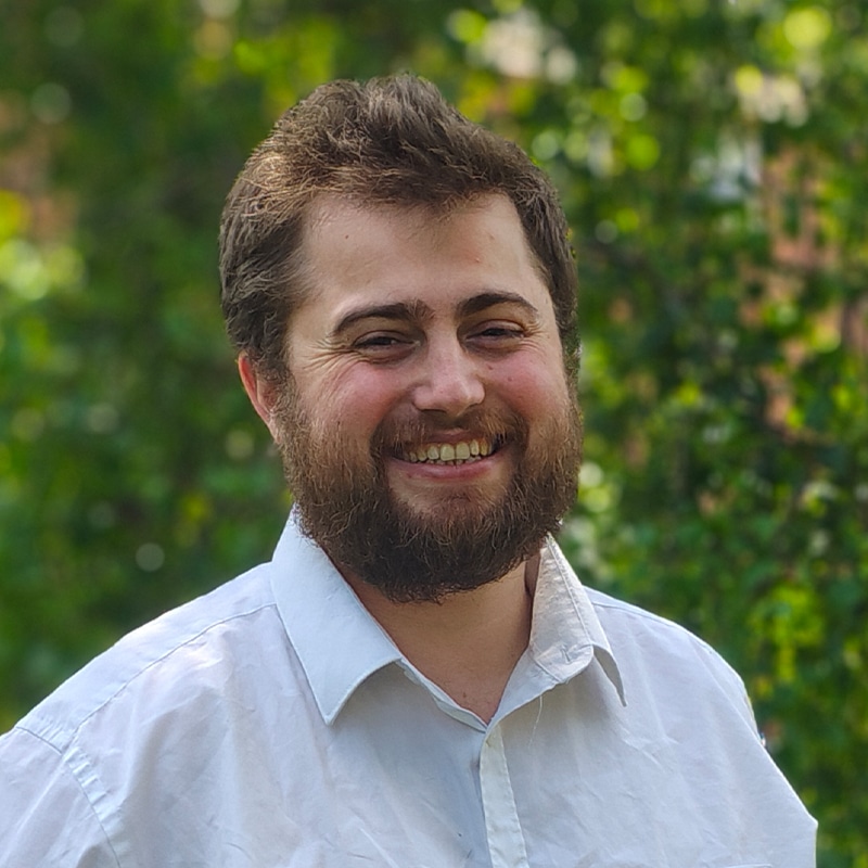 Professional headshot of George Baker, engineering consultant at Create Consulting Engineers, smiling outdoors against green foliage background.