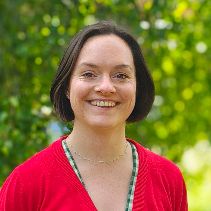 Grace Beard, consulting engineer at Create Consulting Engineers, smiling outdoors with green foliage background.