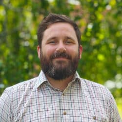 Harry Mansfield, consulting engineer at Create Consulting Engineers, pictured against a blurred green foliage background wearing a checked shirt.