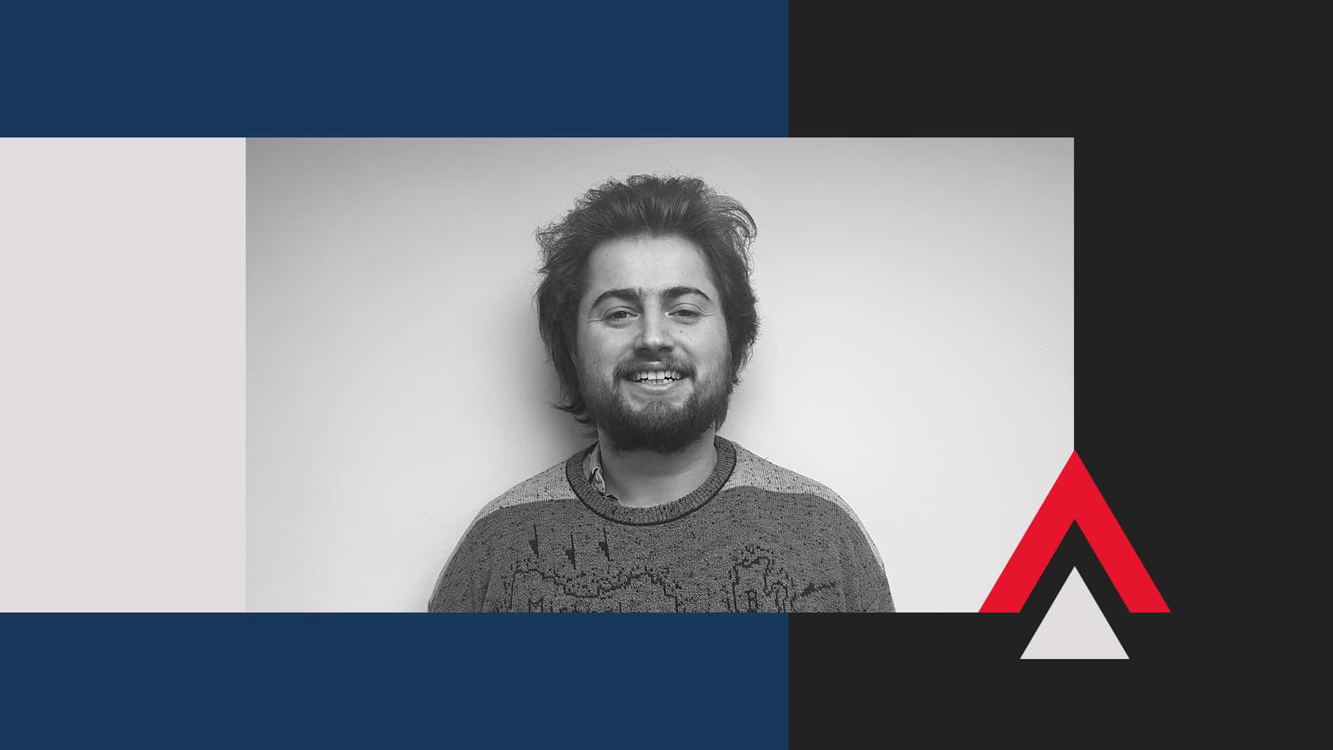 George Baker, a person with short, dark hair and a beard, smiles at the camera, standing against a plain light background with abstract blue, black, and red geometric shapes framing the image.