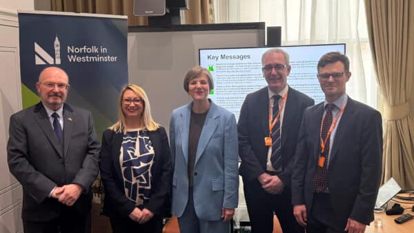 Five people standing indoors in front of a presentation screen displaying "Key Messages." A banner reads "Norfolk in Westminster.