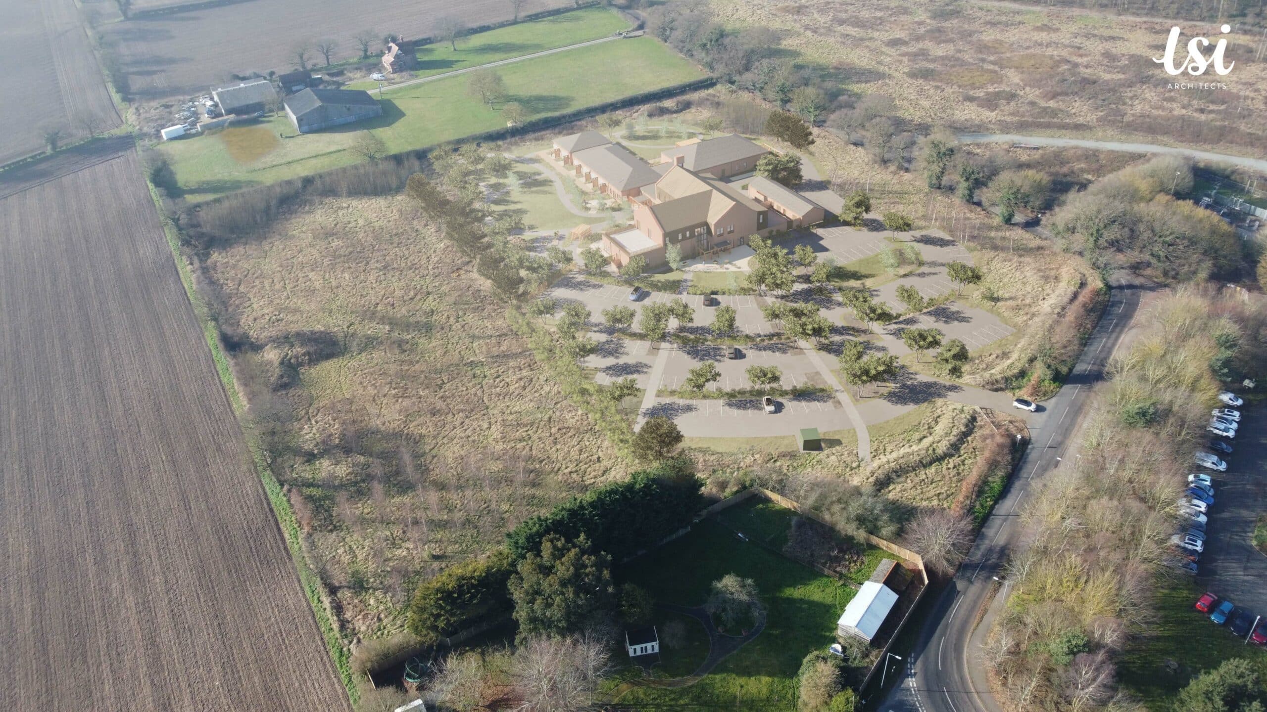 Aerial view of a large building complex surrounded by fields, trees, and roads, with parking lots and several vehicles visible.