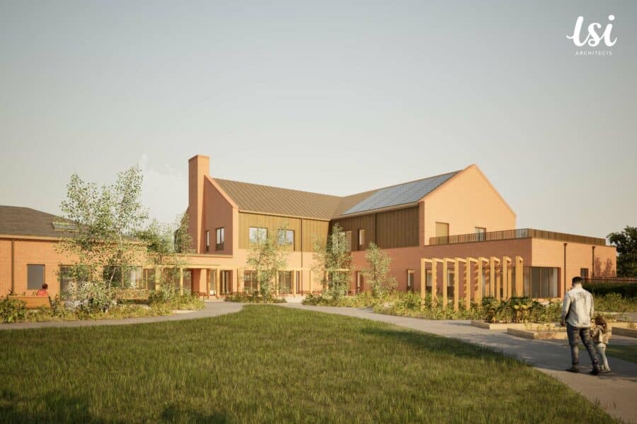 Two people walk on a curved path toward a modern brick building with large windows, a chimney, and landscaped gardens under a clear sky.