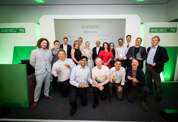A group of people pose on stage holding trophies at an awards event in front of a screen displaying the word "Winners.