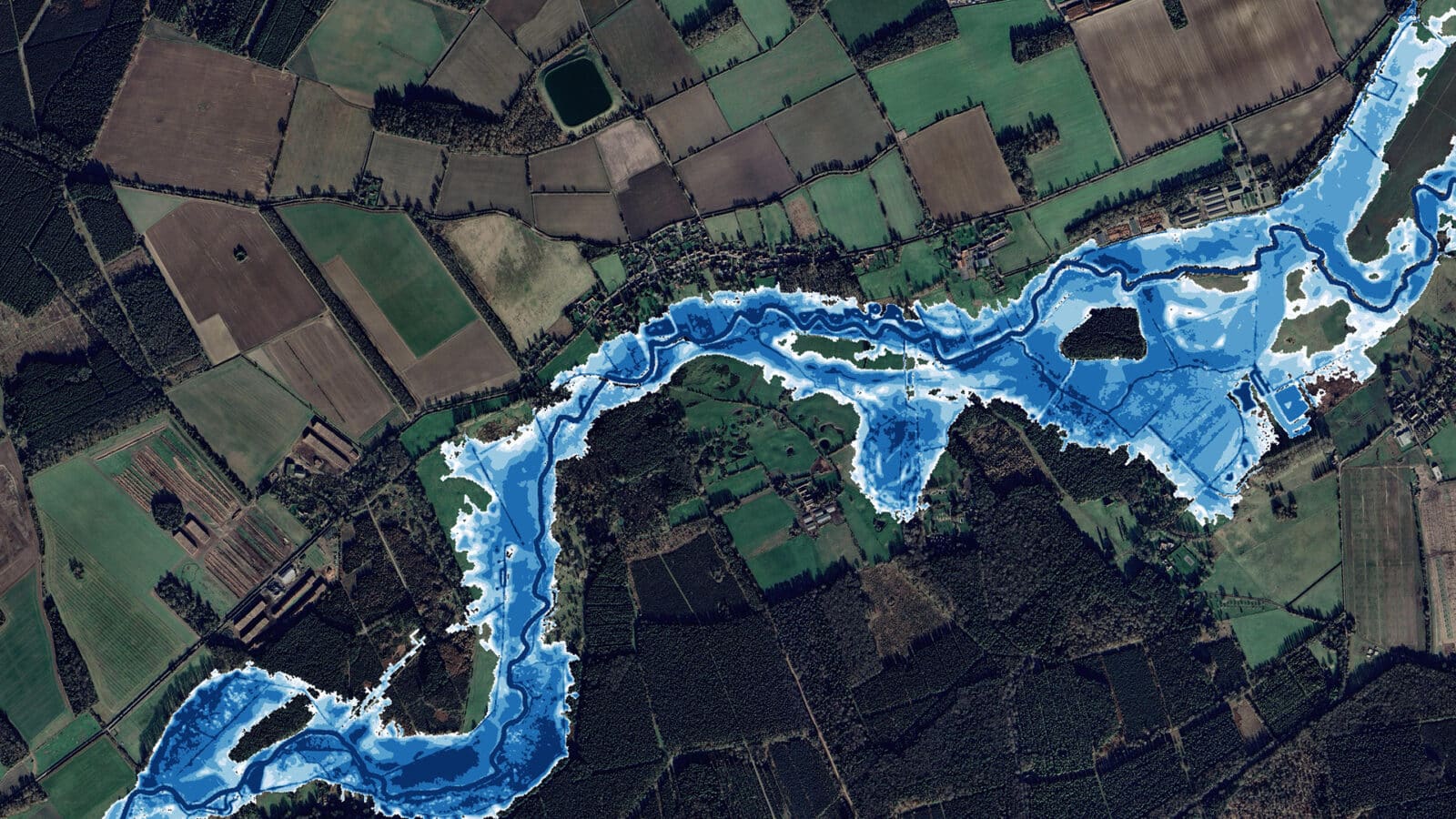 Aerial view of a rural landscape with fields and forests; a river runs through the center, highlighted with blue overlays indicating flood risk zones.