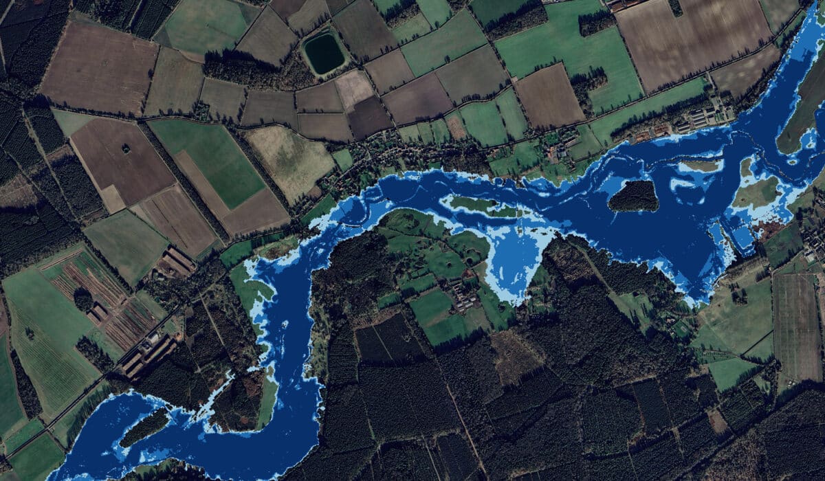 A satellite image shows a river winding through rural farmland and forested areas, with varying shades of blue indicating different water levels or potential flood zones.
