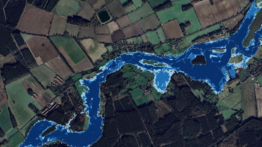 A satellite image shows a river winding through rural farmland and forested areas, with varying shades of blue indicating different water levels or potential flood zones.