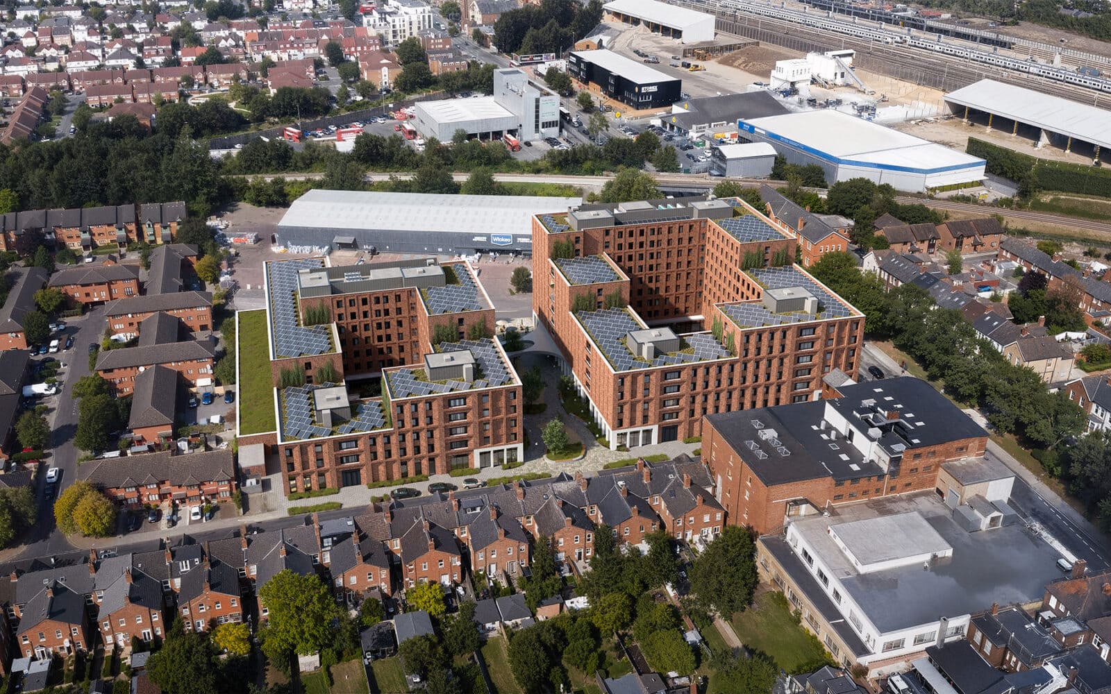 Aerial view of a modern apartment complex near Cricklewood Broadway, featuring brick buildings and surrounded by residential houses, roads, and nearby industrial facilities.