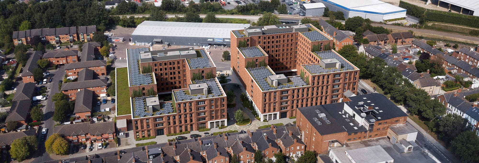 Aerial view of a modern apartment complex near Cricklewood Broadway, featuring brick buildings and surrounded by residential houses, roads, and nearby industrial facilities.