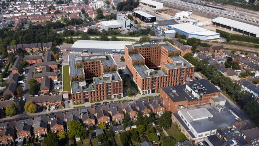 Aerial view of a modern apartment complex near Cricklewood Broadway, featuring brick buildings and surrounded by residential houses, roads, and nearby industrial facilities.
