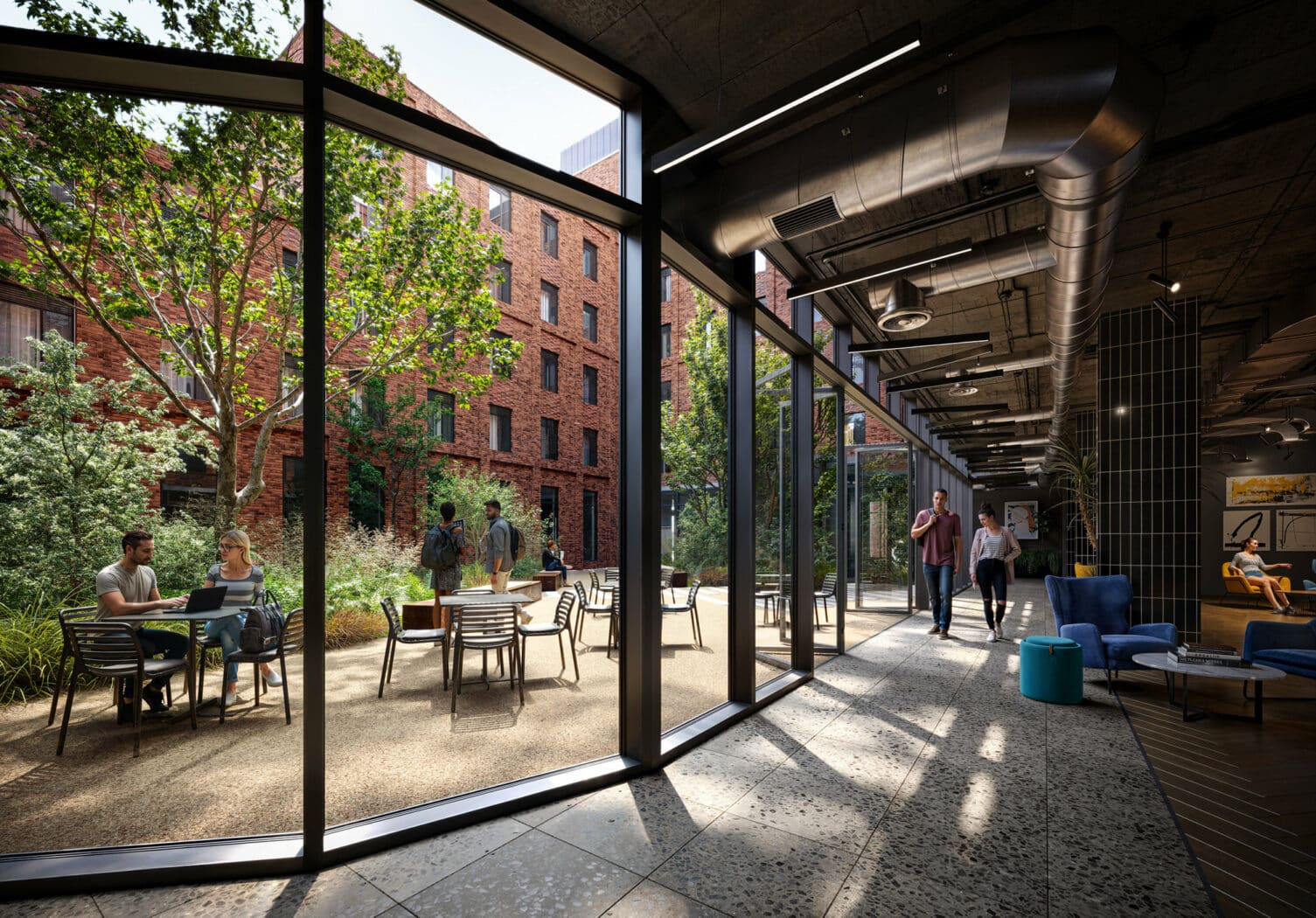 People sitting and talking at outdoor tables in a courtyard with red brick buildings, seen through large glass windows from a modern indoor lounge area.