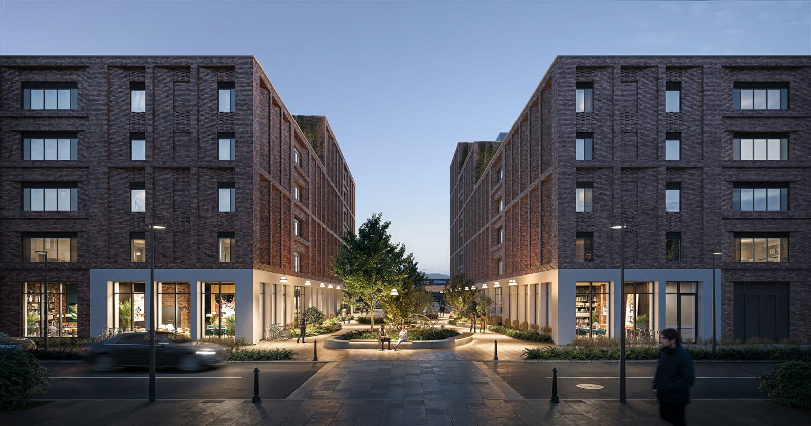 Two modern brick apartment buildings face each other across a landscaped courtyard with trees and benches at dusk; storefronts line the ground floors, and people walk along the street.
