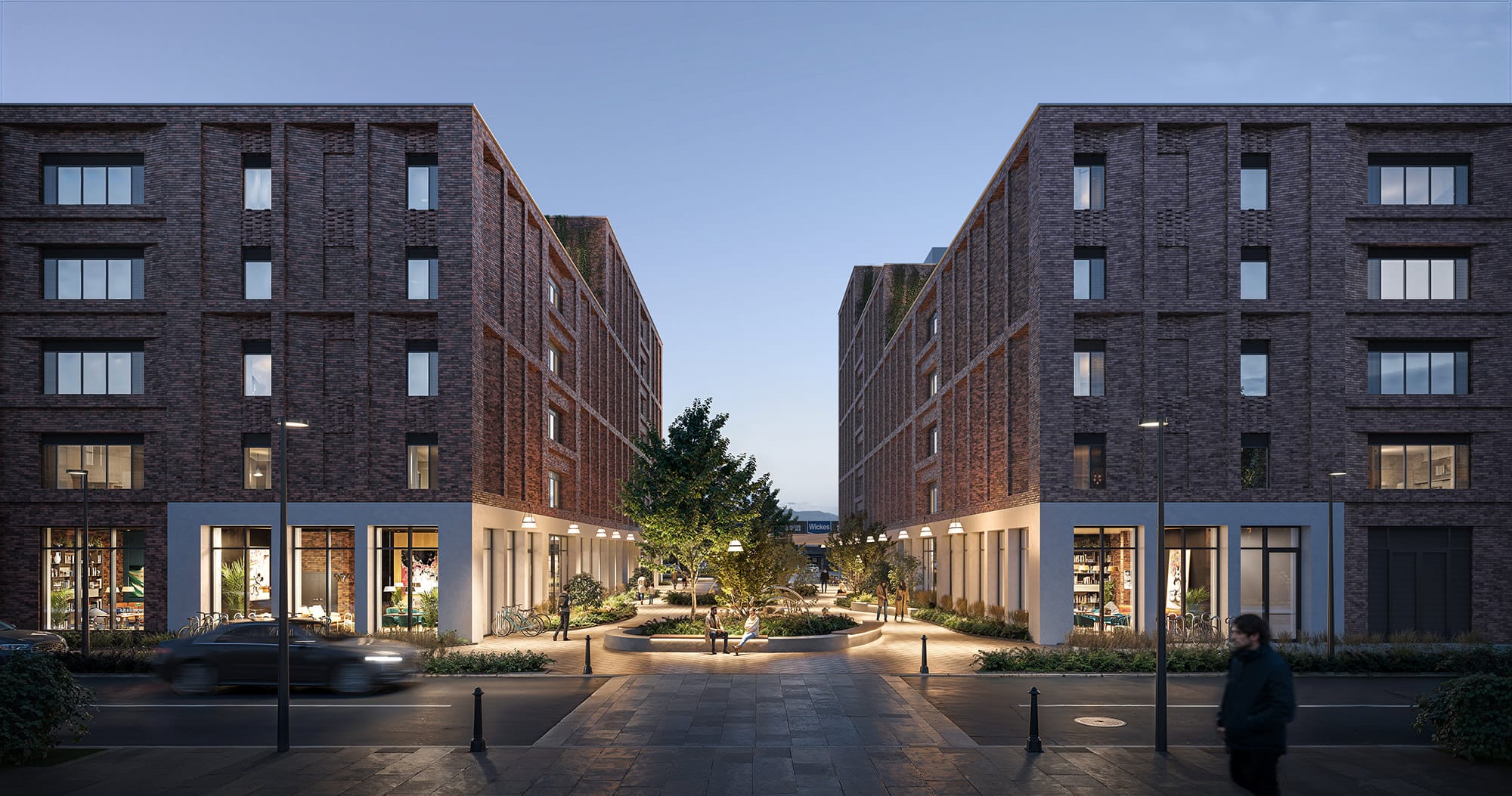 Two modern brick apartment buildings face each other across a landscaped courtyard with trees and benches at dusk; storefronts line the ground floors, and people walk along the street.