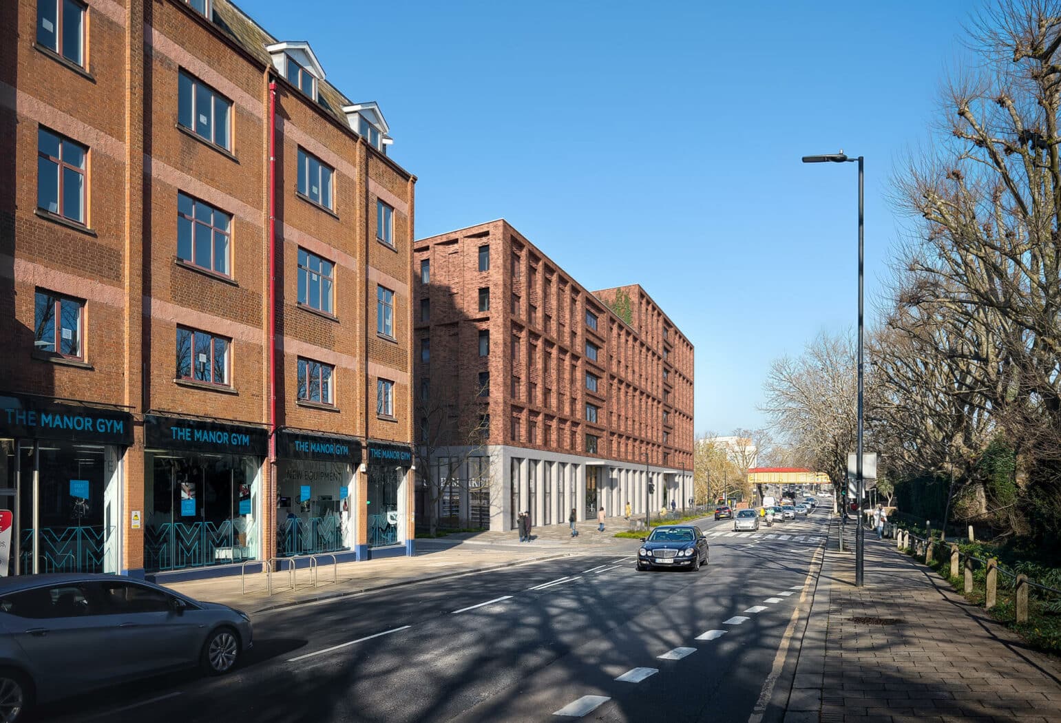 A wide city street with cars parked and driving, lined with brick buildings and a gym, under a clear blue sky.