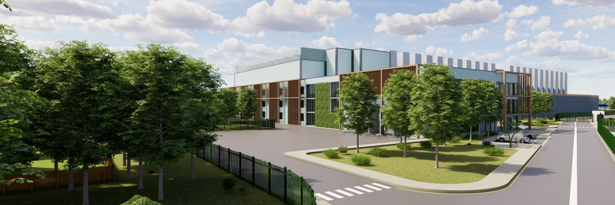 Modern building with a glass facade surrounded by trees, a lawn, and parking area under a partly cloudy sky. A crosswalk and fence are visible in the foreground.