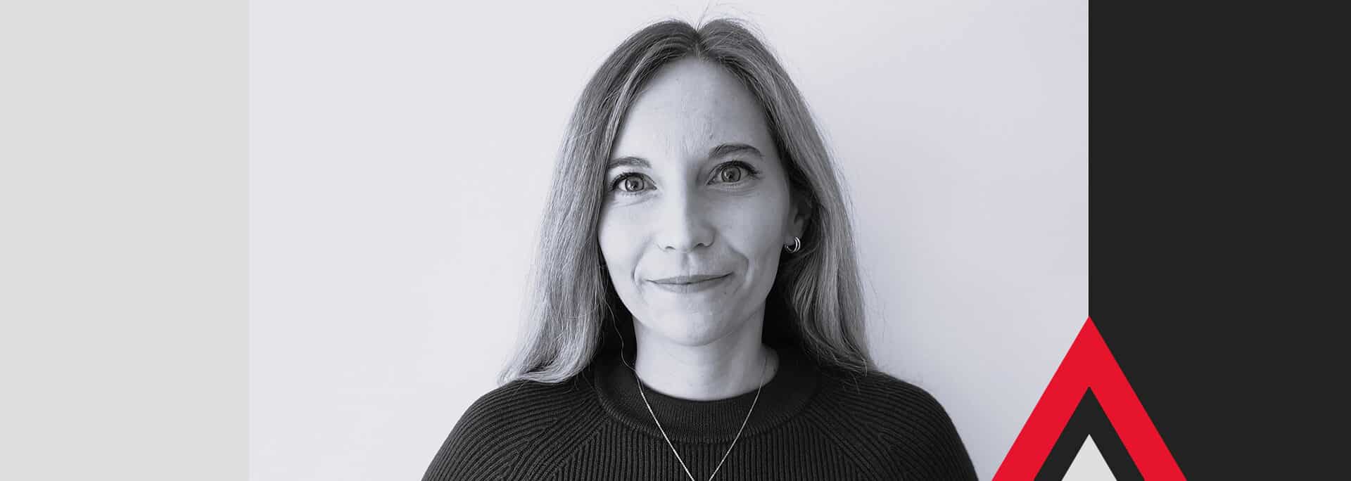 A woman with straight, shoulder-length hair and a slight smile faces the camera. The background features geometric shapes in blue, black, gray, and red.