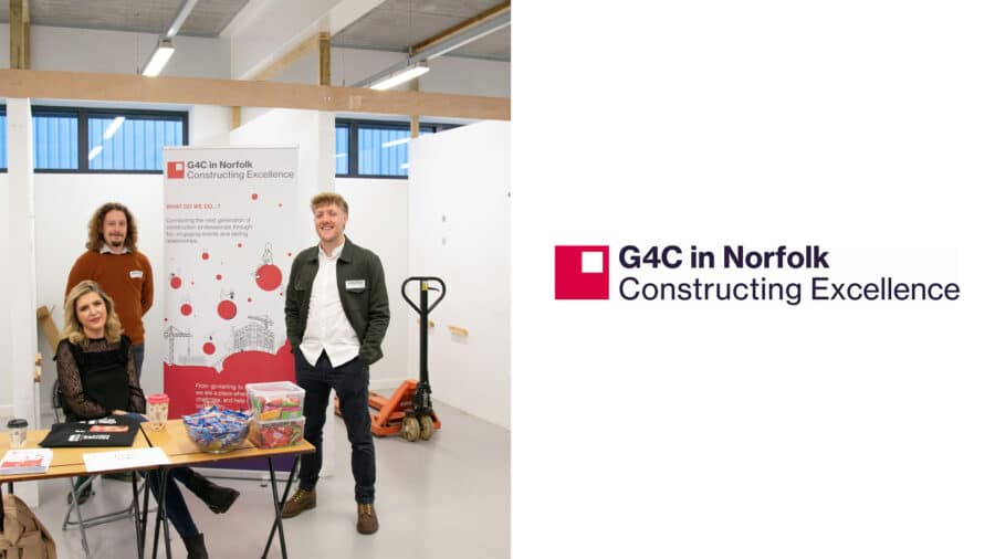 Three people stand and sit at a promotional table for G4C Norfolk at Constructing Excellence, featuring informational materials and a G4C banner in a modern indoor space.