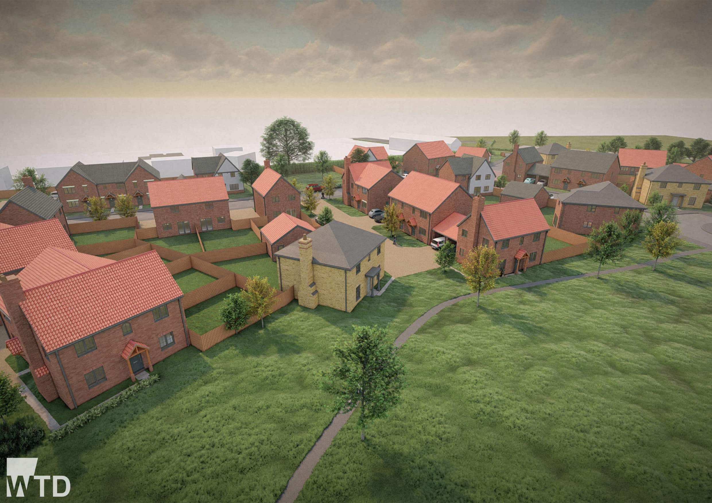 Aerial view of Buxton’s suburban residential neighborhood with detached houses, red and tan roofs, fenced yards, trees, and a grassy open area in the foreground.