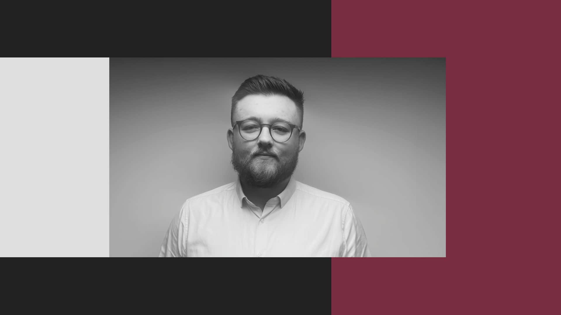 A man with glasses and a beard poses in front of a plain background, framed by geometric color blocks in black, white, and burgundy.