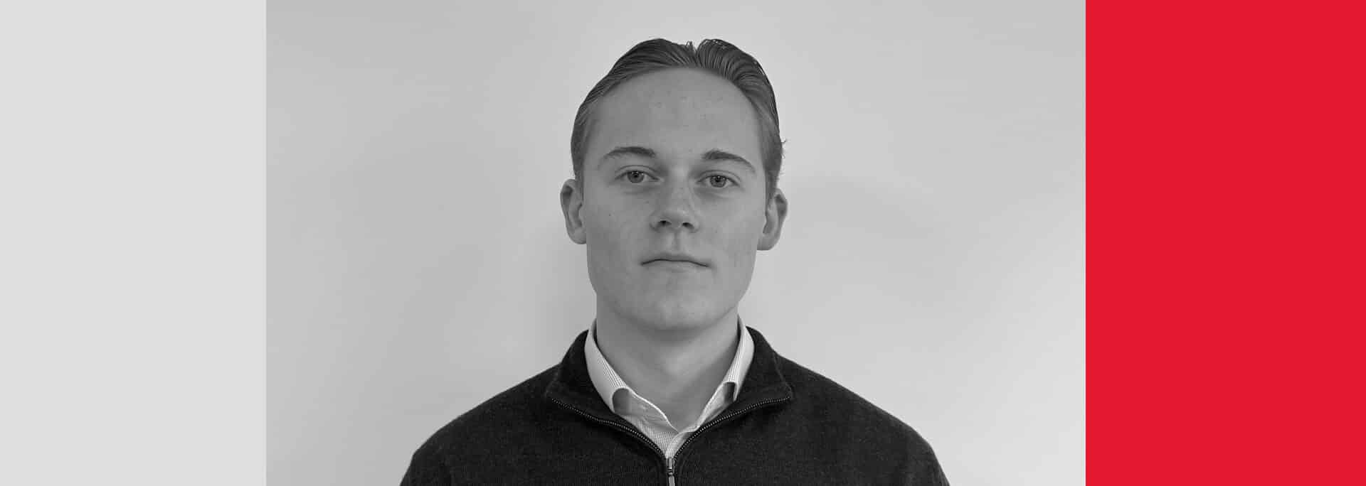 A young man with short, neatly styled hair and a collared shirt stands against a plain white background, framed by geometric blocks of black, white, and red.