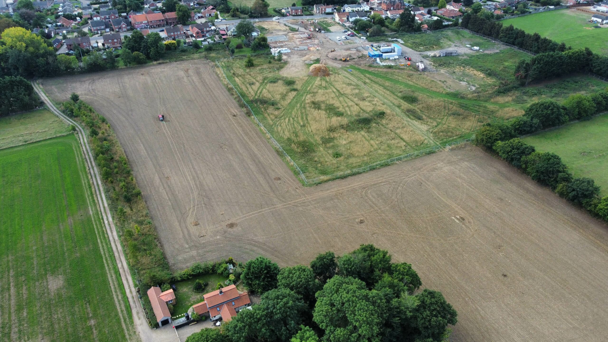 Aerial view of farmland with ploughed and unploughed fields, a few scattered buildings, and a small cluster of houses in the background.