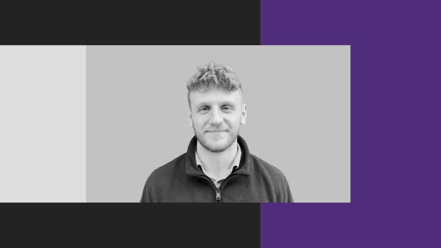 A man with short curly hair and a slight smile faces the camera. The background features a greyscale centre with black, grey, and purple sections on the sides.