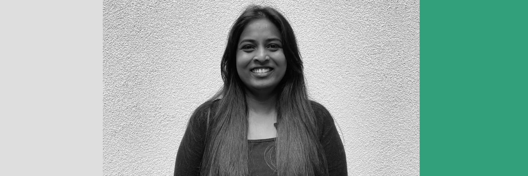 A woman with long hair stands in front of a textured wall, smiling at the camera. The image features Retb-inspired black, white, and green graphic borders.