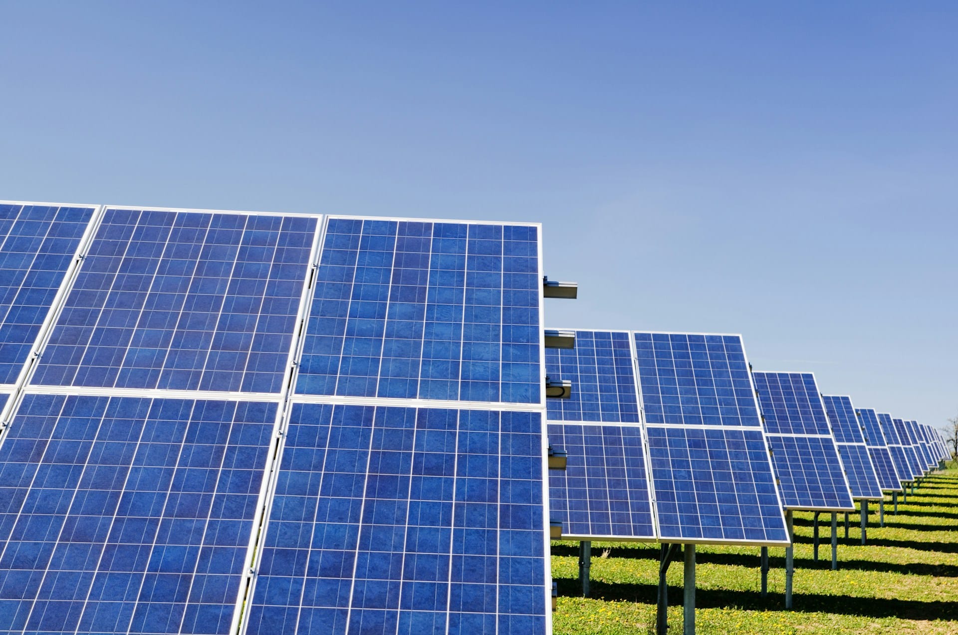 Rows of blue solar panels are installed on metal frames in a grassy field under the clear Malshanger sky.