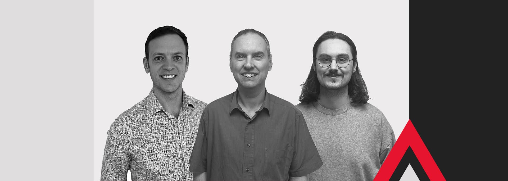 Three men standing side by side, smiling, in front of a geometric background with red, black, white, and grey shapes and a stylised red and white arrow graphic.