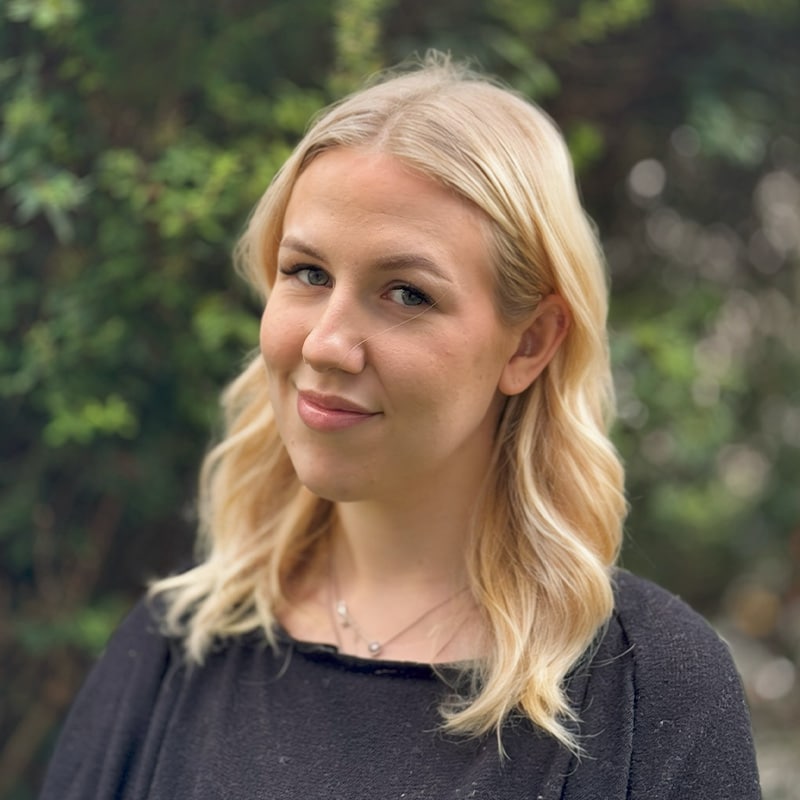 Leah, a new starter at Create Consulting Engineers, poses outdoors against a green foliage background.